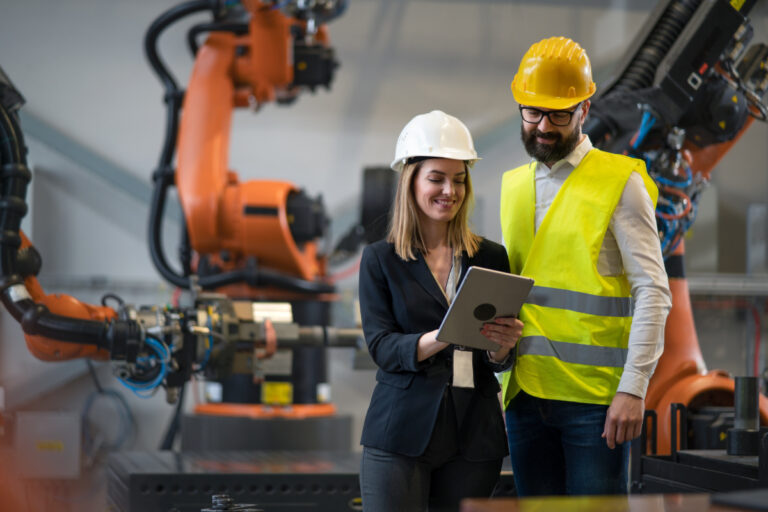 Chief engineer and project manager in modern industrial factory with robot arms looking at a tablet too help illustrate manufacturing industry.